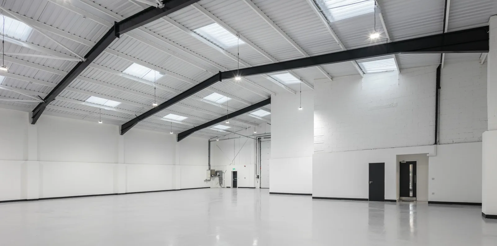 Refurbished industrial unit with a light grey resin floor, white walls and exposed steel roof beams