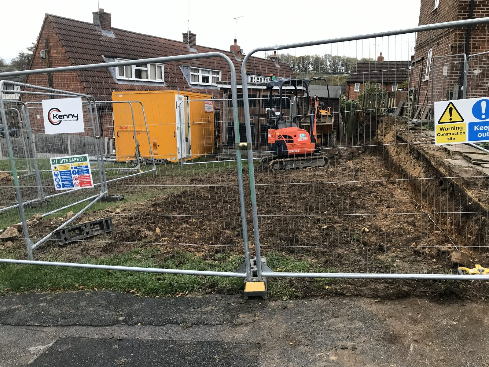 Fenced site with PT Kenny Construction signage, welfare unit and mini excavator
