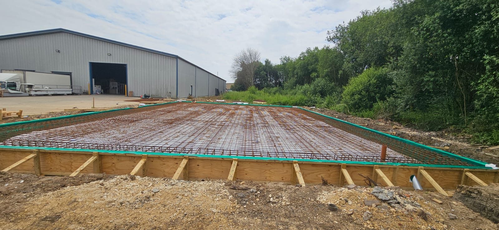 Large reinforced slab with steel mesh inside timber formwork beside a commercial unit